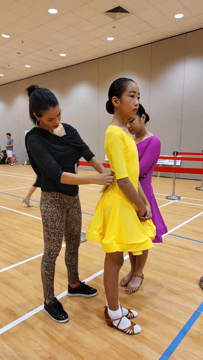 Raliza adjusting a young student's arm position during a class in a school sports hall