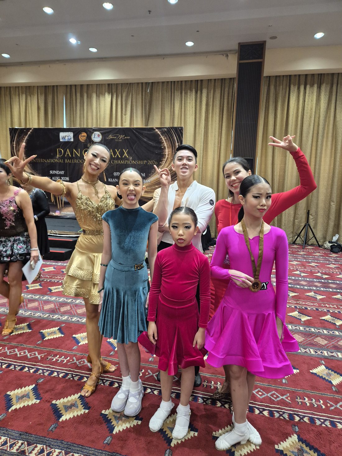Young students in colourful Latin dresses posing together in a hotel ballroom after a competition