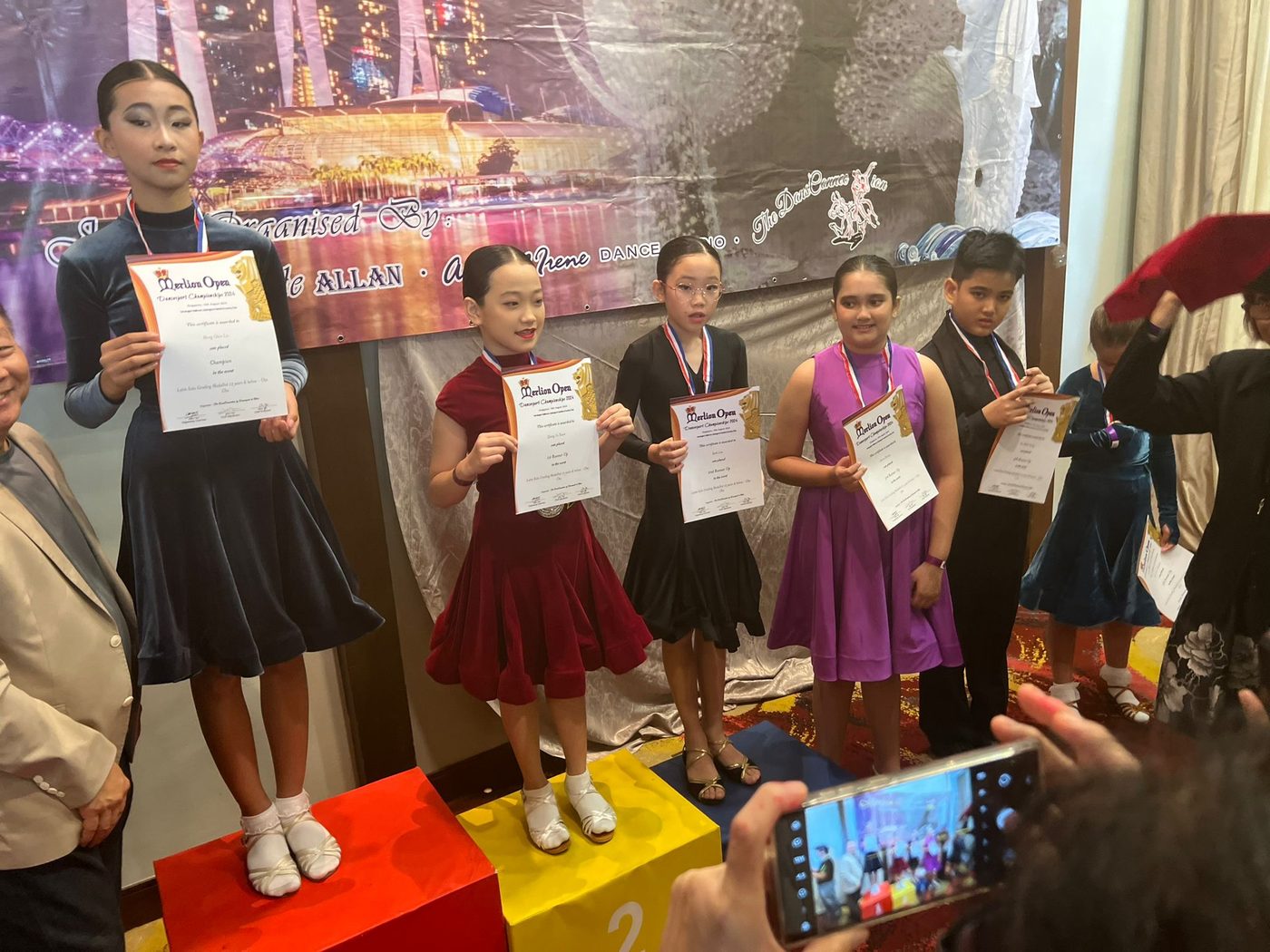 Young students on a podium holding certificates after a school dance competition