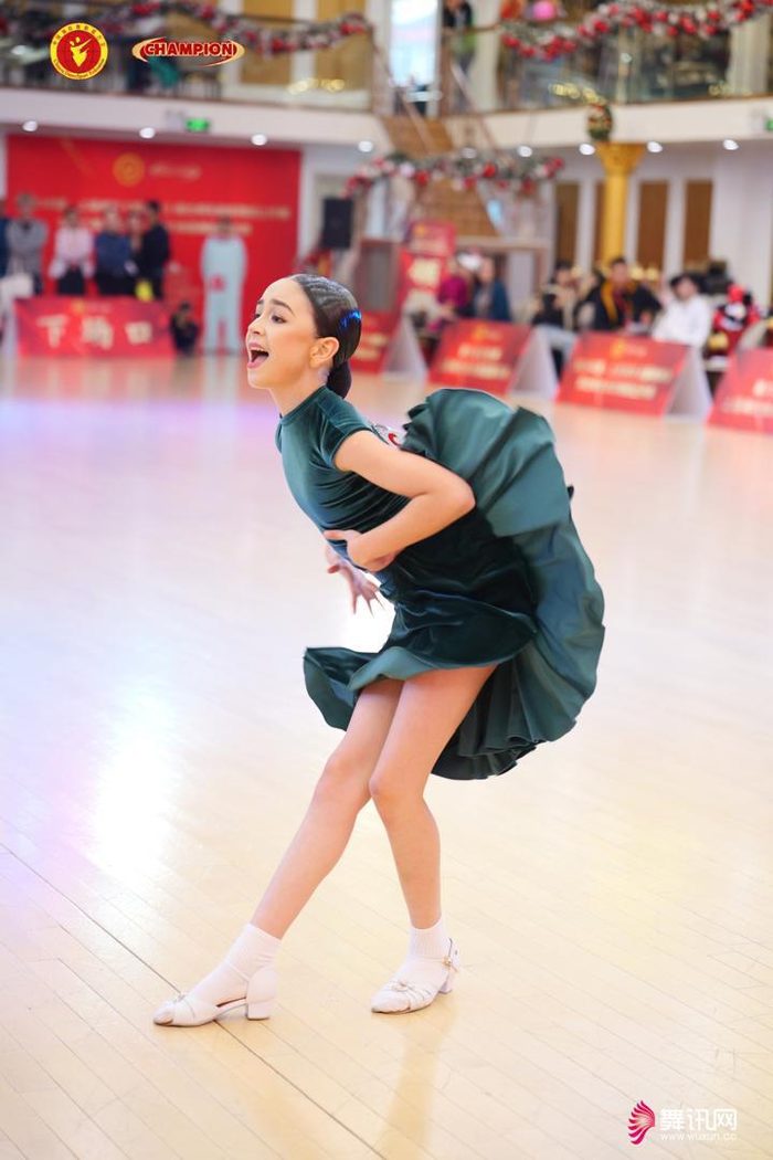 A young dancer in a green dress performing a Latin solo at a competition