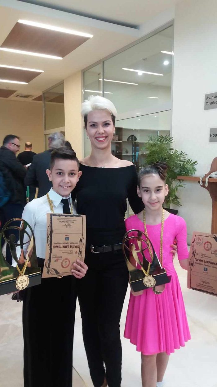 Two young dancers in competition outfits each holding a trophy