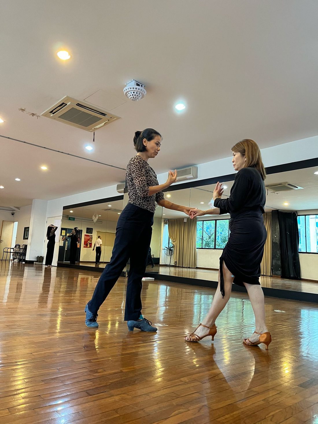 Raliza guiding an adult student's arm position during a private lesson in a bright studio