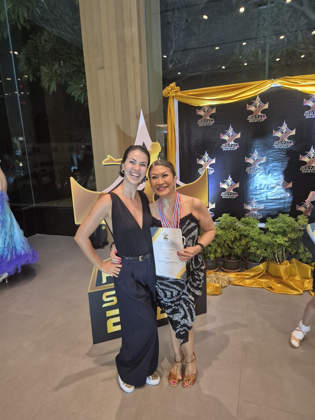 Raliza and a student with a certificate in front of the Royal Siam Cup backdrop