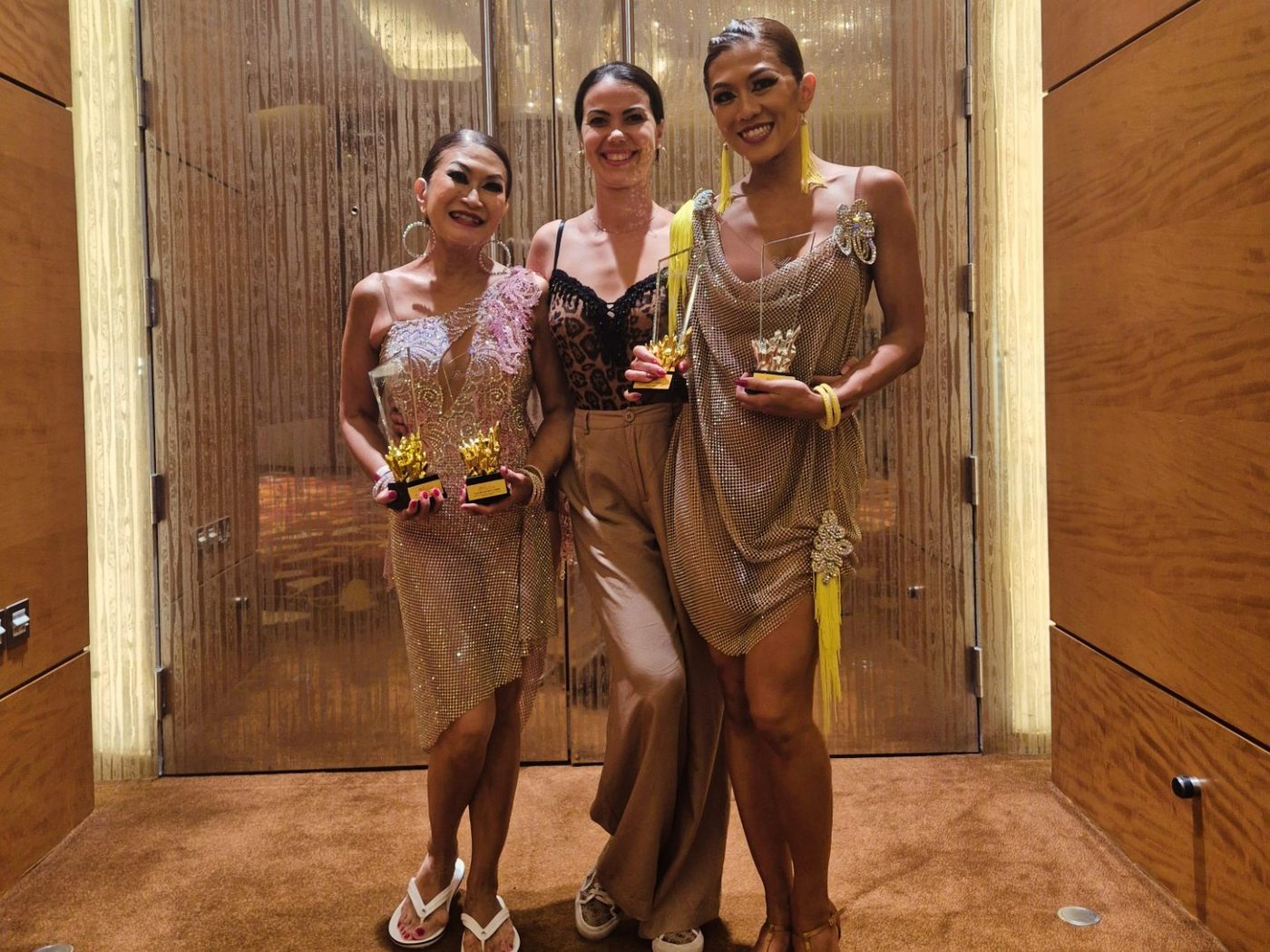 Raliza with two adult students, each holding a trophy after a competition